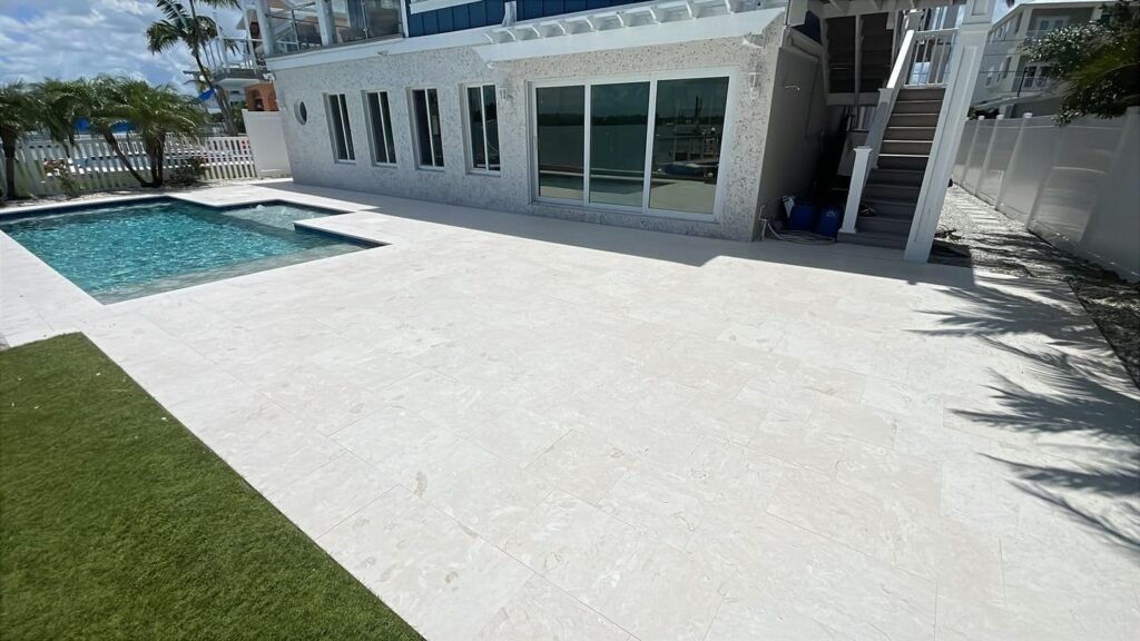 Completed white travertine pool deck beside a canal-side residential pool in Tampa Bay