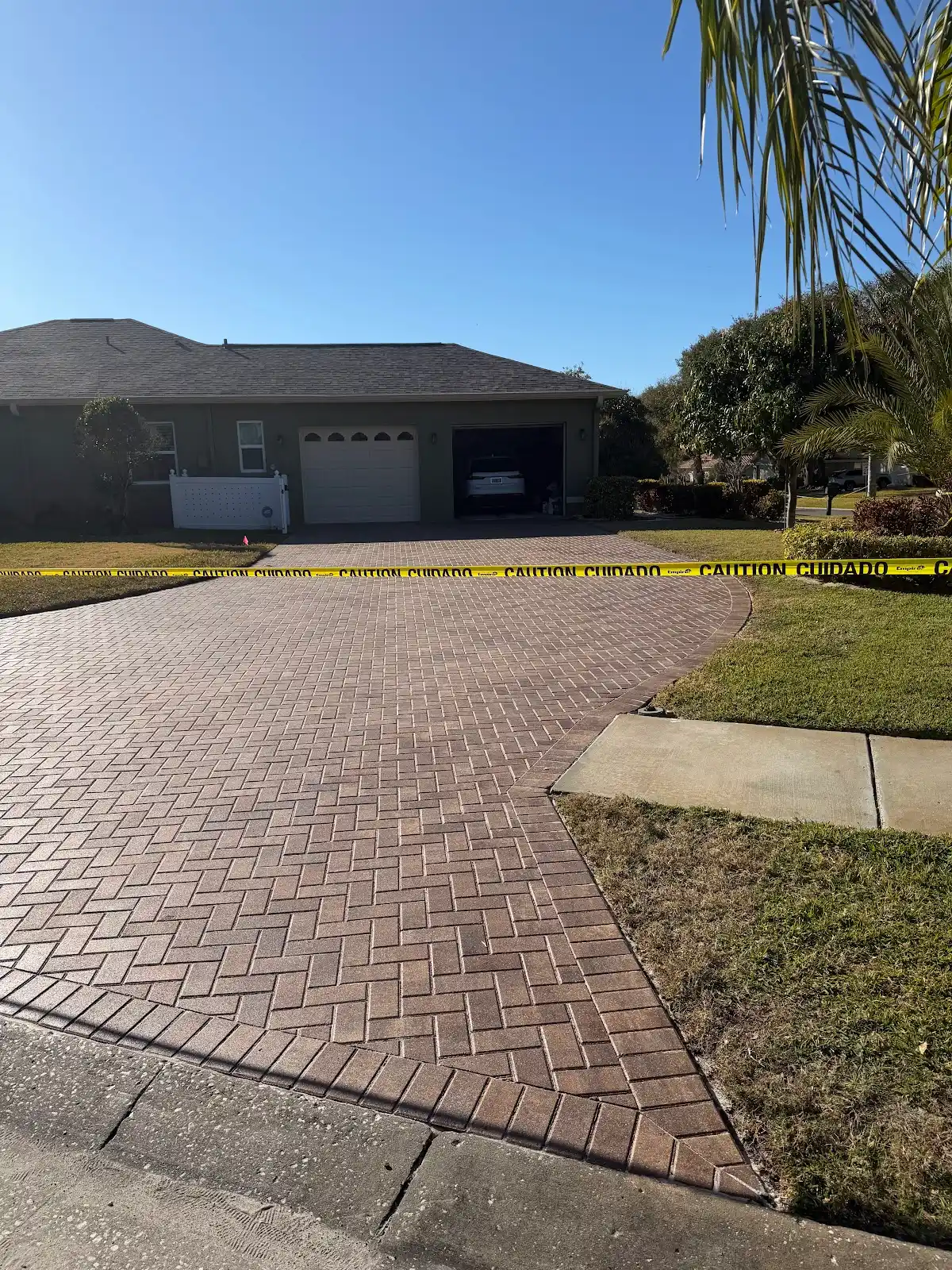Newly finished brick paver driveway leading to a two-car garage with caution tape across the driveway.