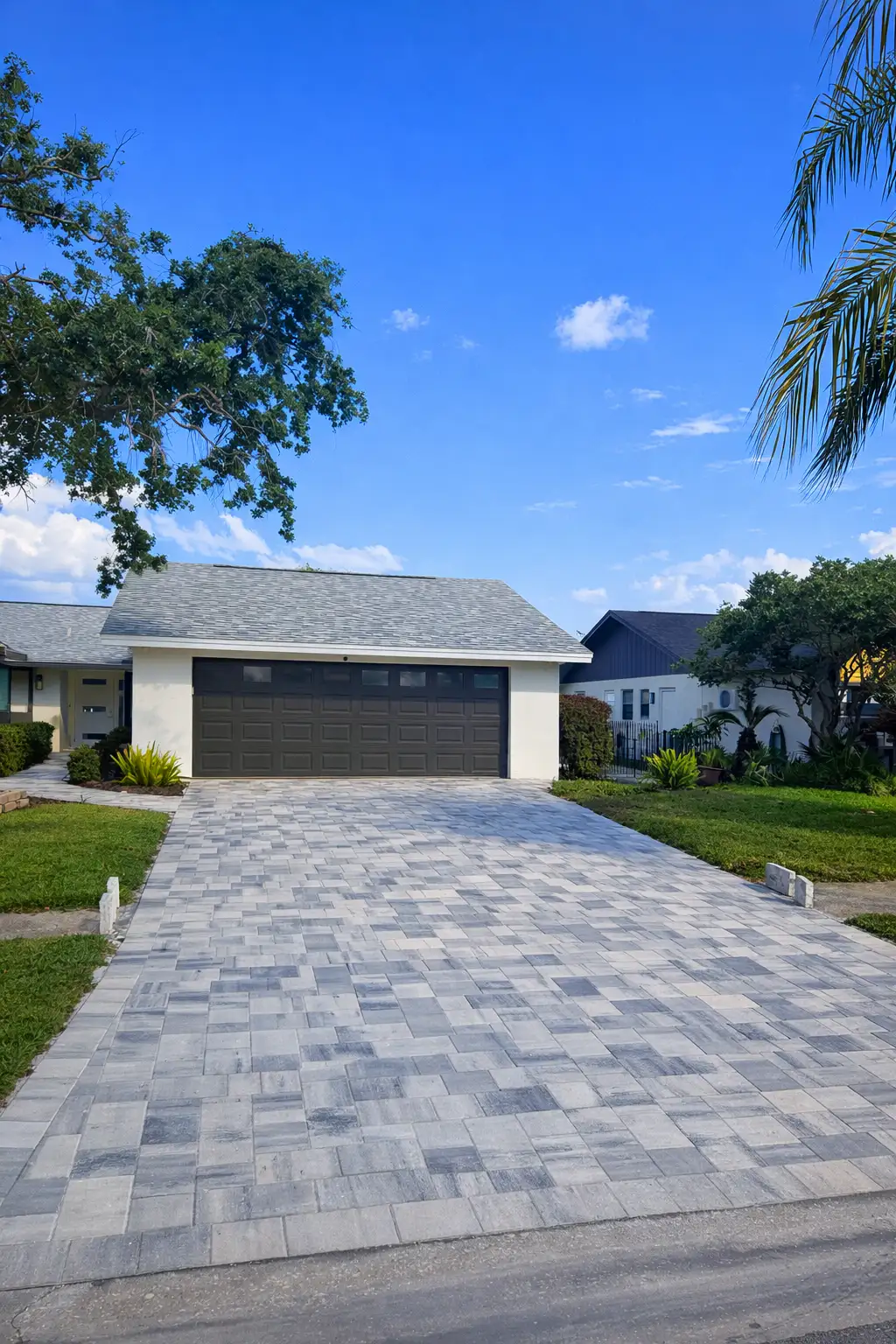 Newly installed patterned gray paver driveway in front of a two-car garage under clear blue sky