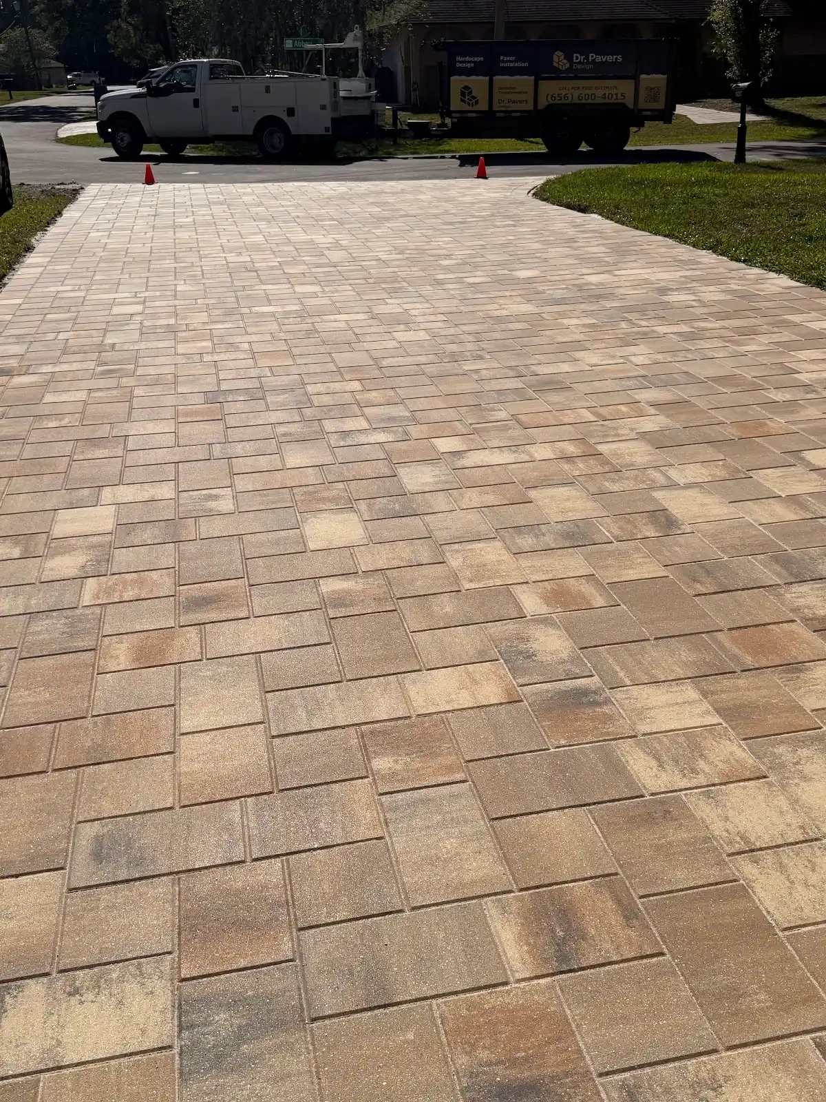 Beige and brown patterned paver driveway freshly installed with utility trucks in the background on a sunny day