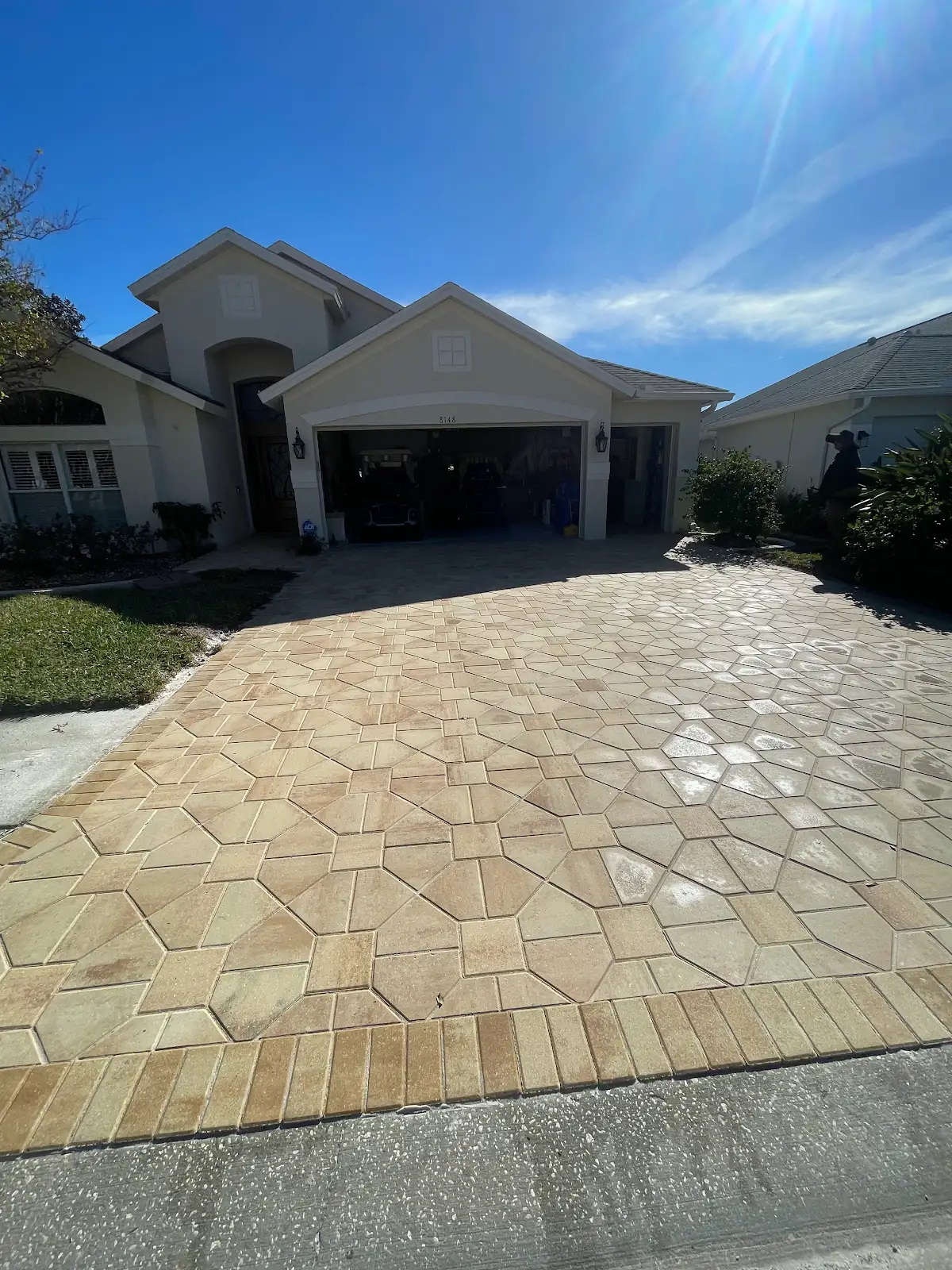 Newly installed geometric patterned paver driveway in front of a residential garage with clear blue sky.
