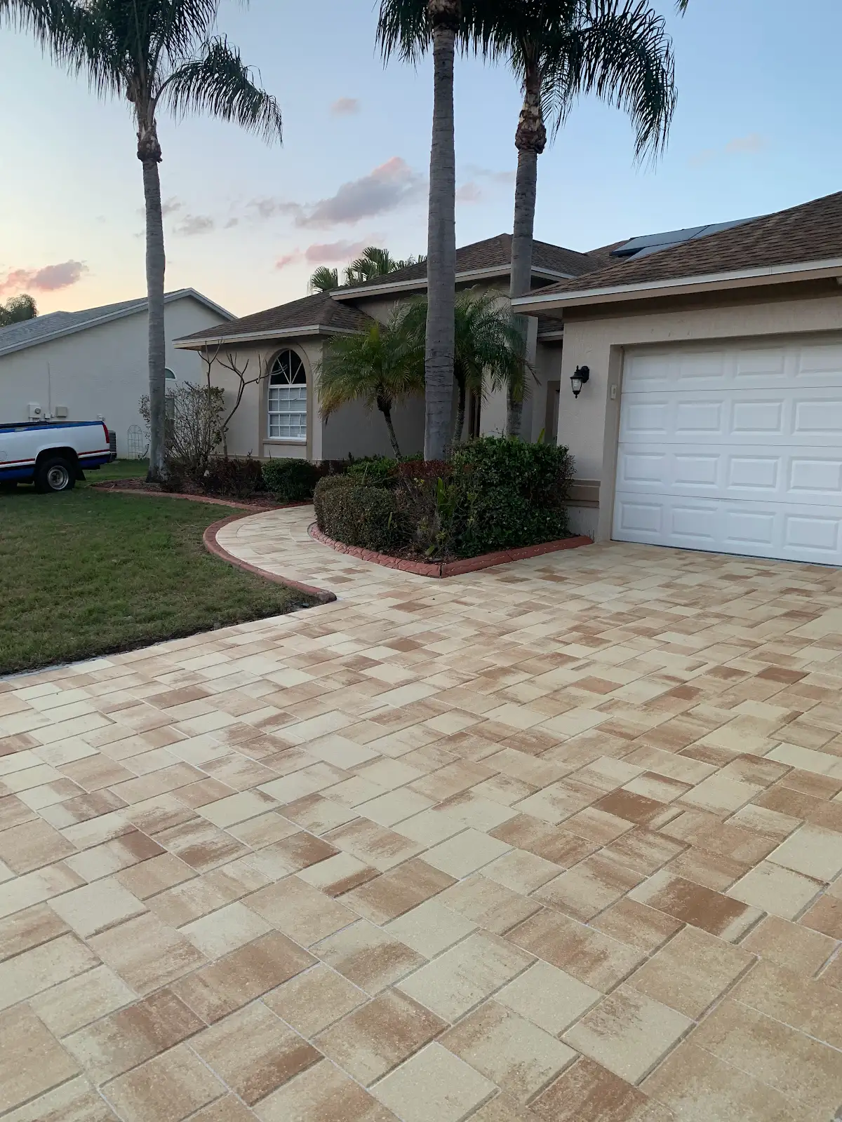 Beige and brown paver driveway and curved walkway with landscaping in front of a single-story house with a garage in Tampa Bay