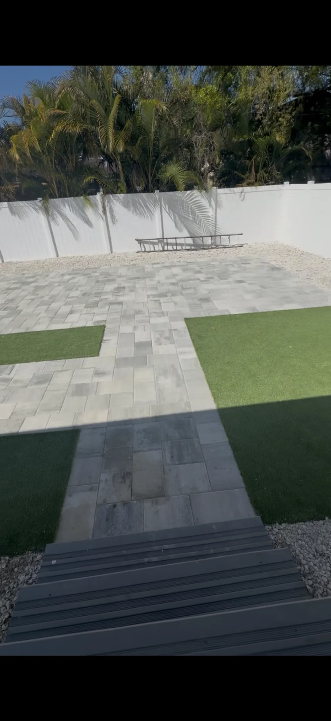 Completed gray paver patio with turf accent squares and white privacy fence in Tampa Bay
