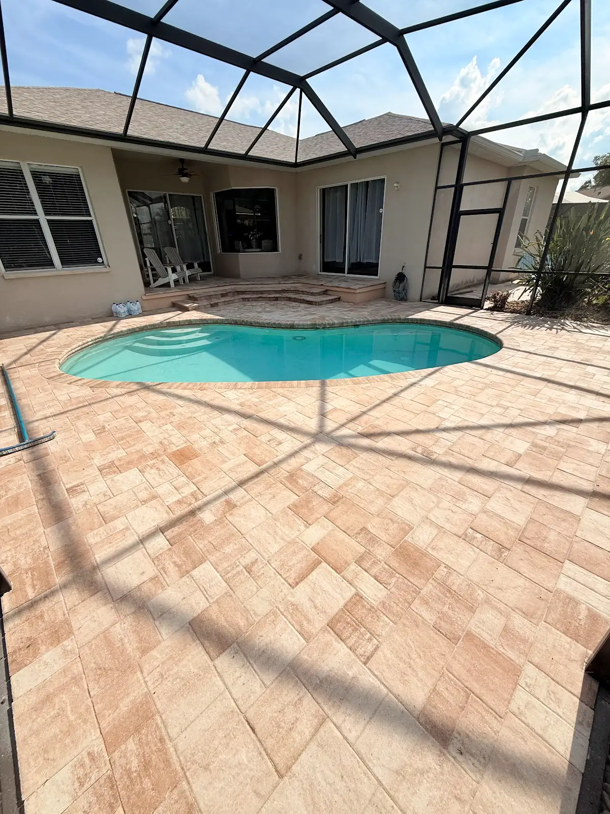Swimming pool surrounded by newly installed light beige paver pool deck with screened enclosure overhead in Tampa Bay Florida