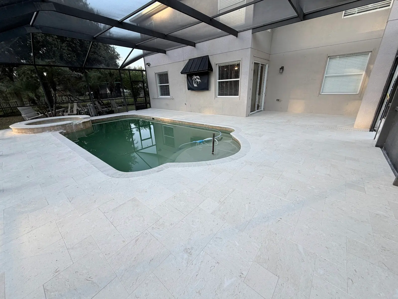 Light-colored travertine marble pool deck and spa surround with kidney-shaped pool under screened enclosure