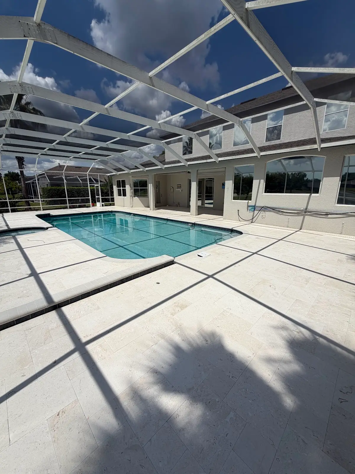 Swimming pool with light travertine marble tile deck and white enclosure structure casting shadows