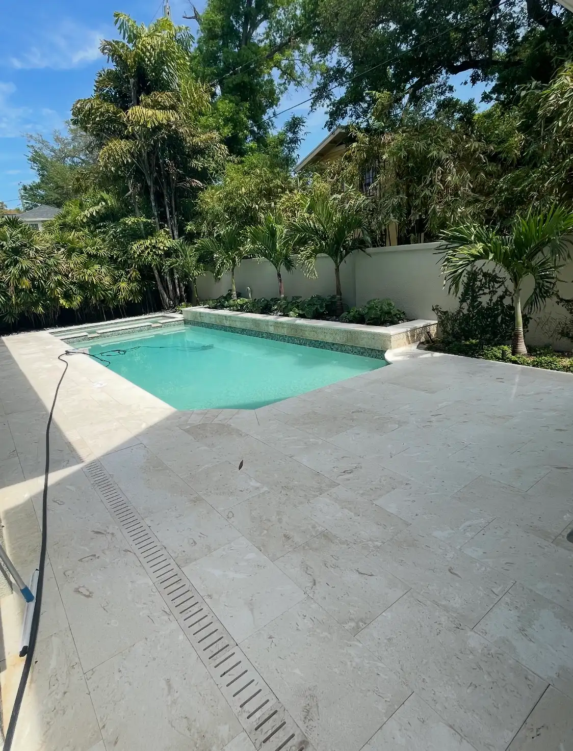 Travertine marble pool deck around a swimming pool with tropical plants and clear blue sky