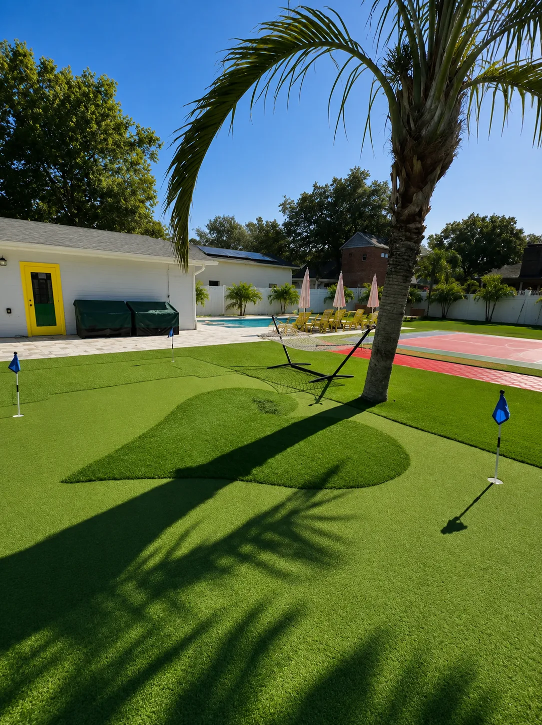Completed backyard putting green with a palm tree, pool, hammock, and colorful recreation court