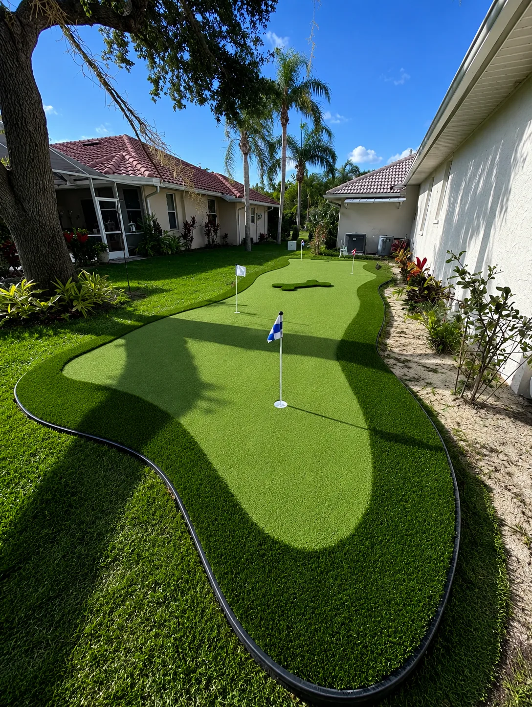 Completed narrow side yard putting green with curved dark turf borders between two homes