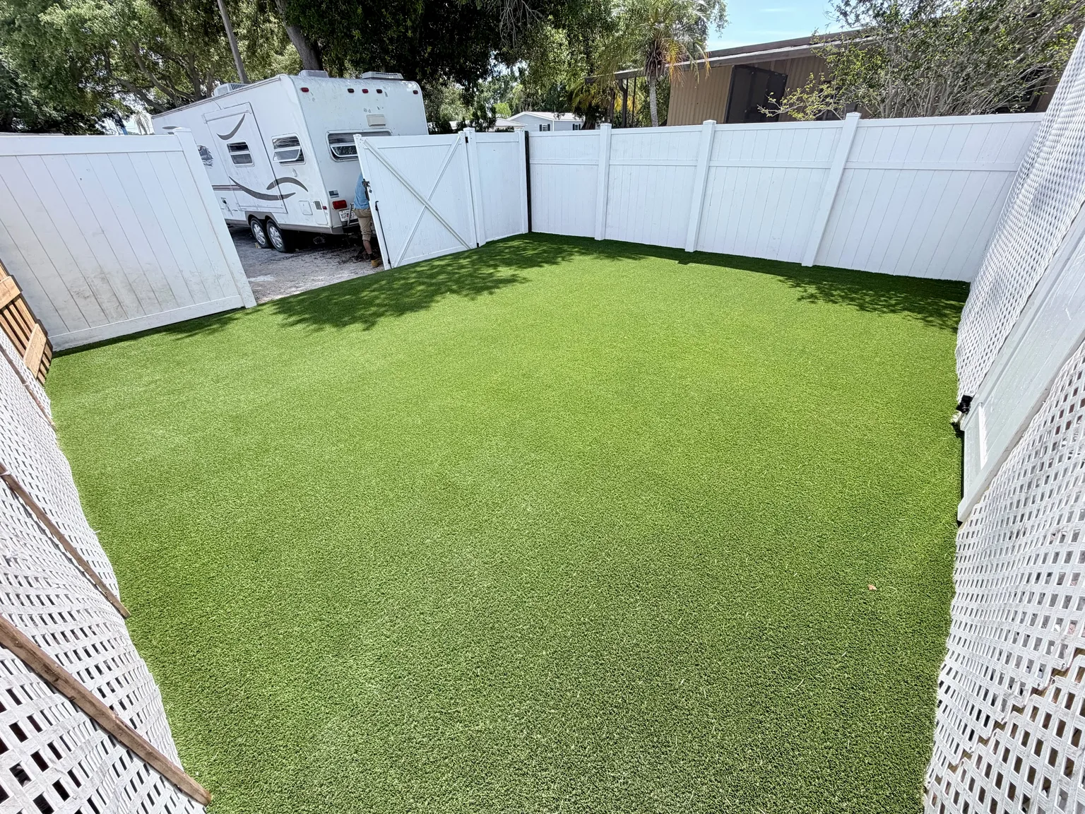 Completed rectangular artificial turf yard enclosed by a white vinyl fence beside a home