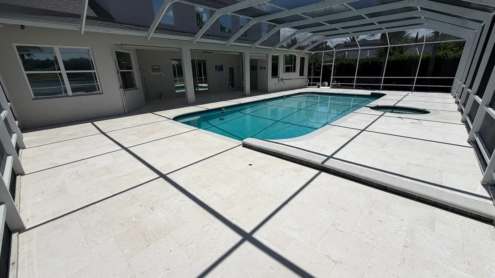 Light-colored travertine pool deck around a screened residential swimming pool in Tampa Bay