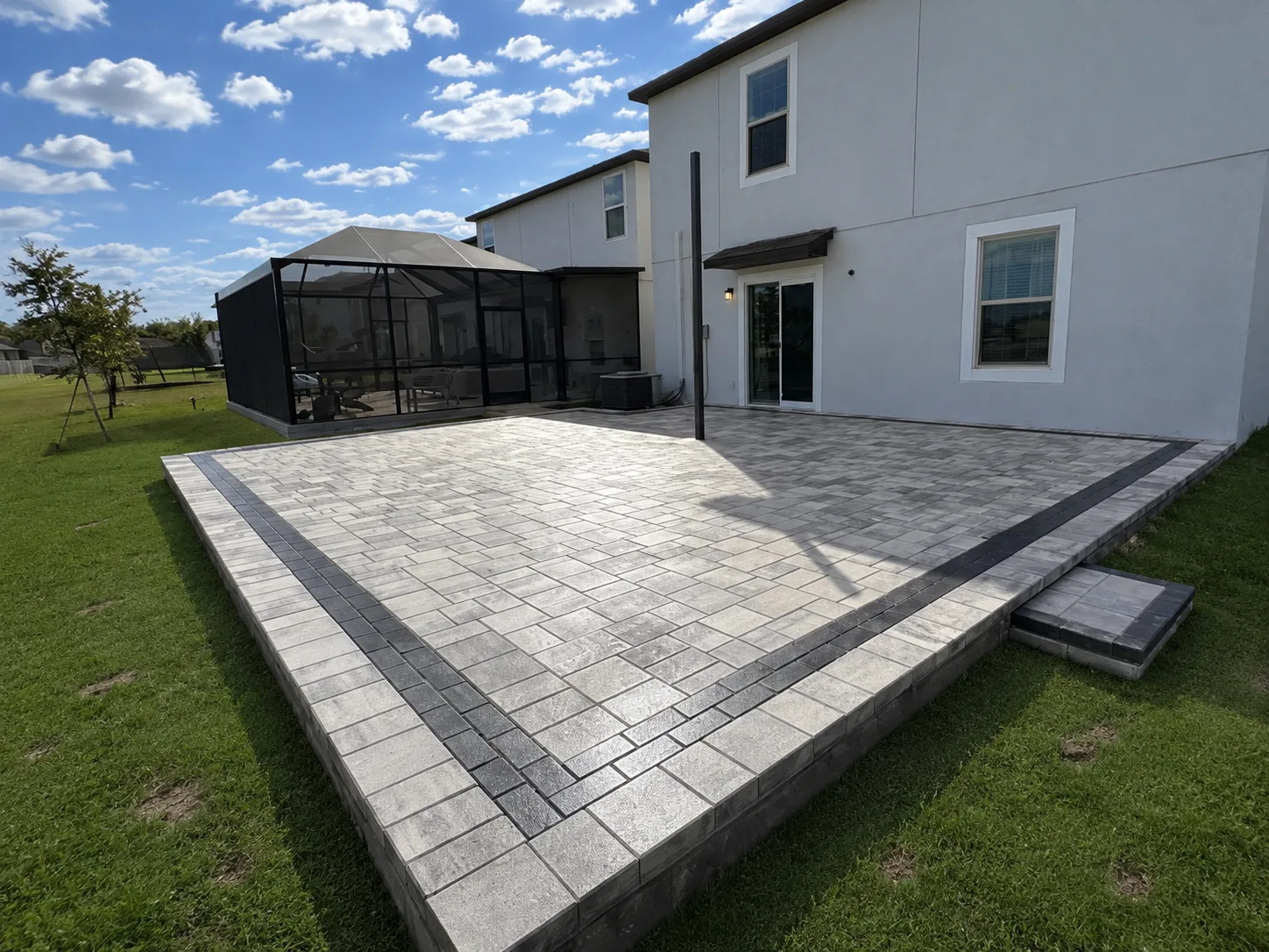 Elevated gray paver patio with a dark border behind a Tampa Bay home