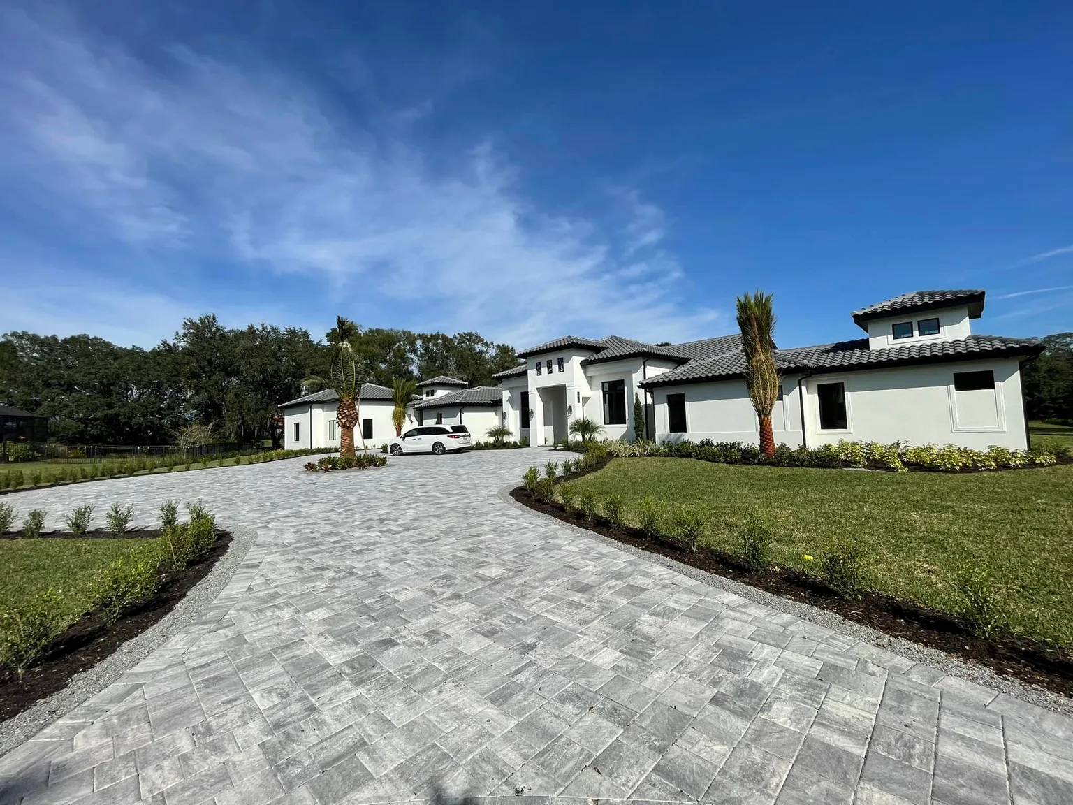 Wide modern gray paver driveway leading to a white Tampa Bay home