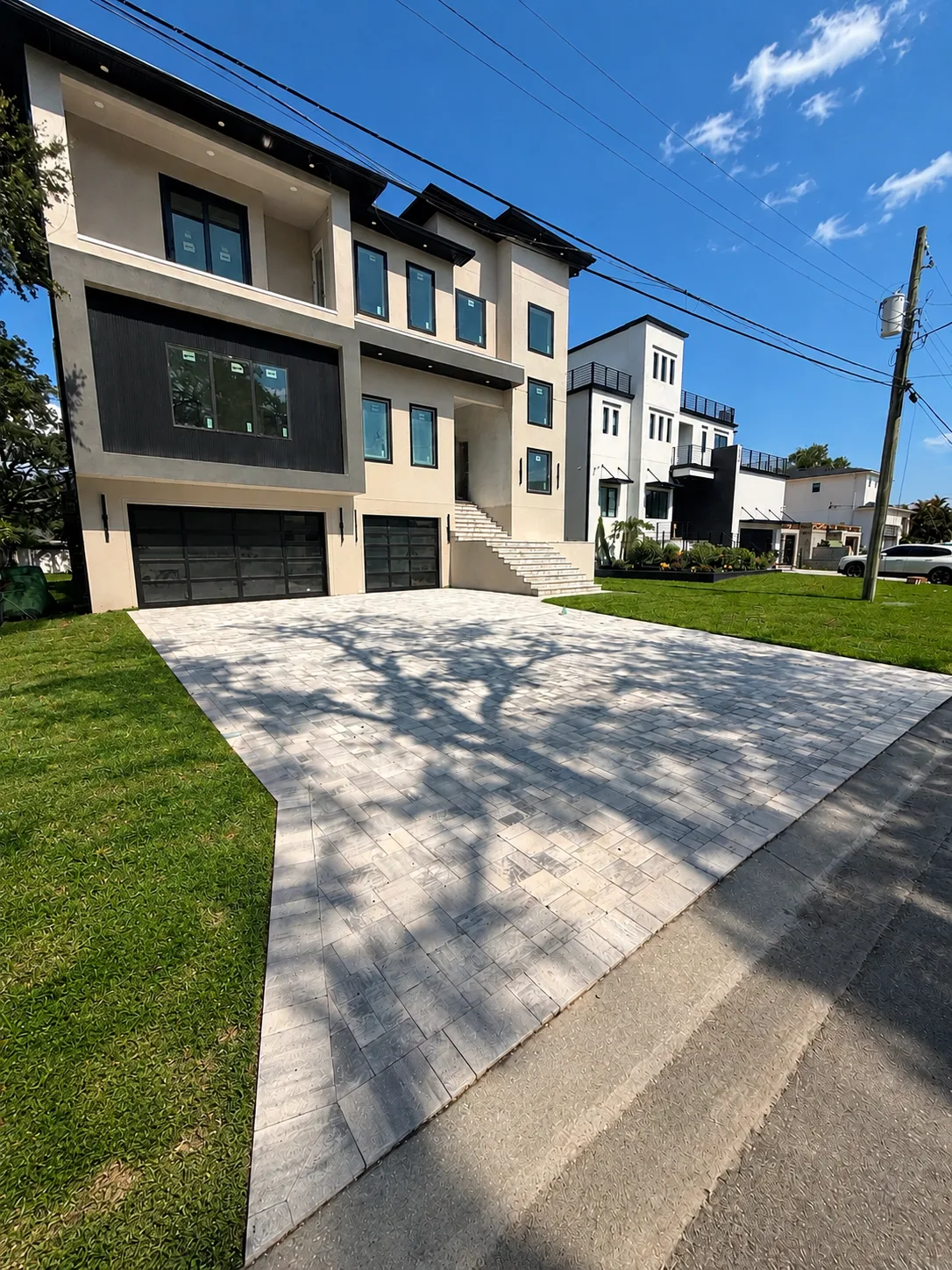 Completed light gray paver driveway in front of a modern multi-story home