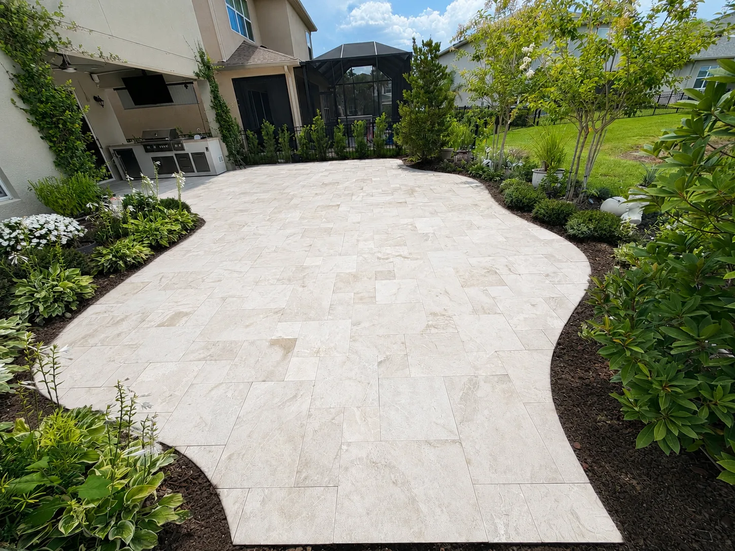 Curved light marble walkway bordered by fresh landscaping and artificial turf beside a residence