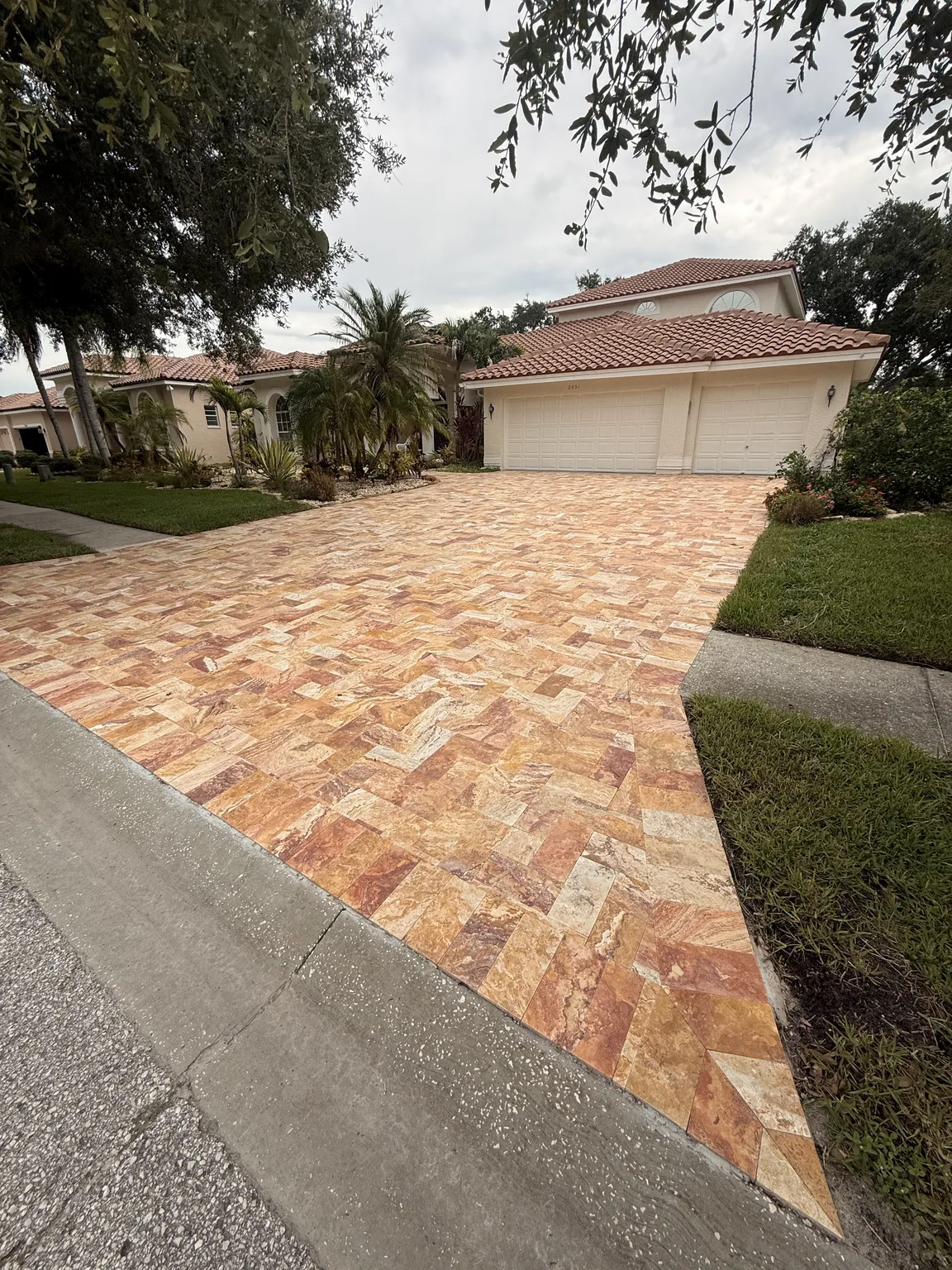 Completed warm tan and rust travertine driveway leading to a residential garage