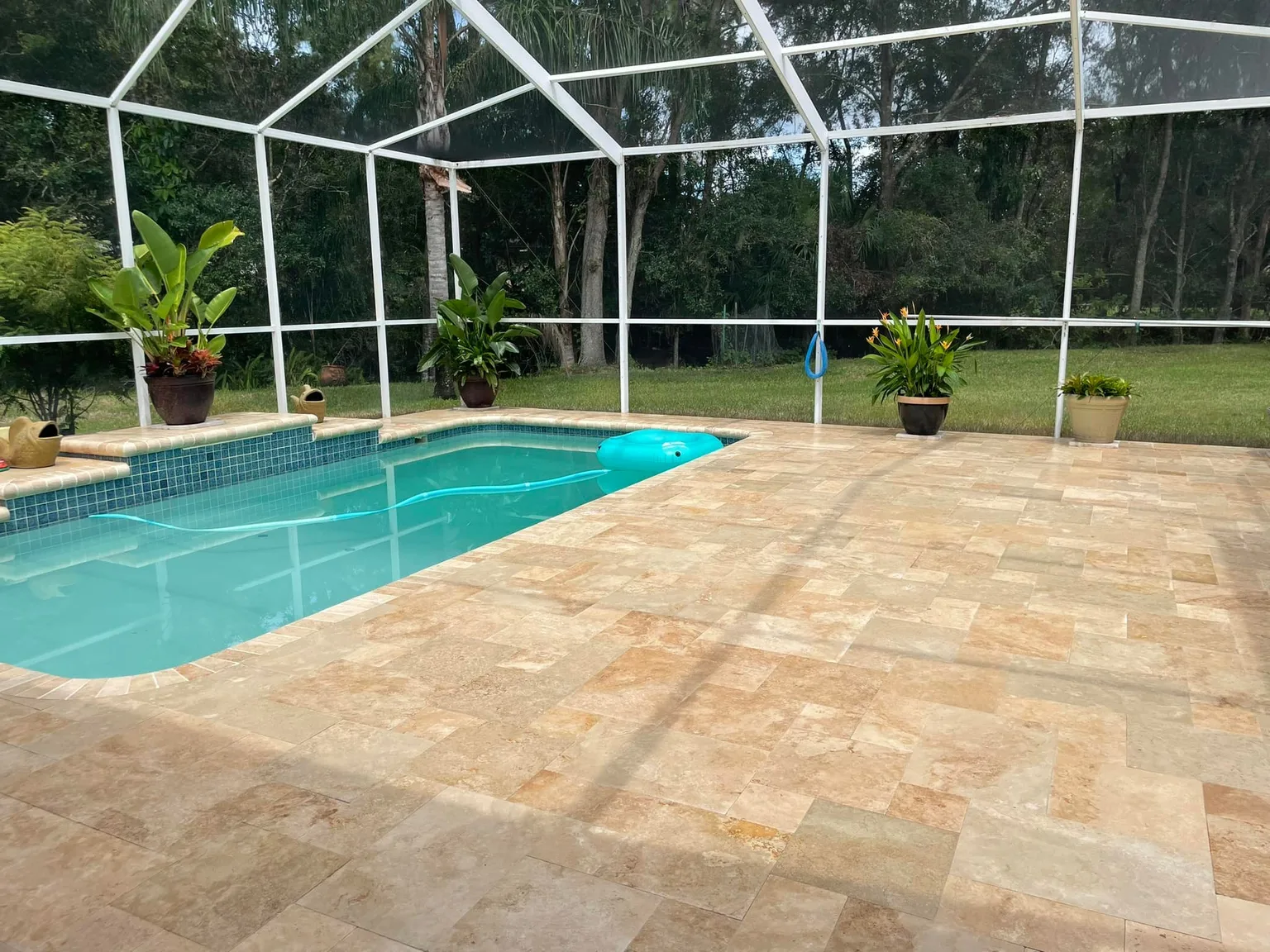 Completed travertine pool deck around a screened swimming pool in Tampa Bay