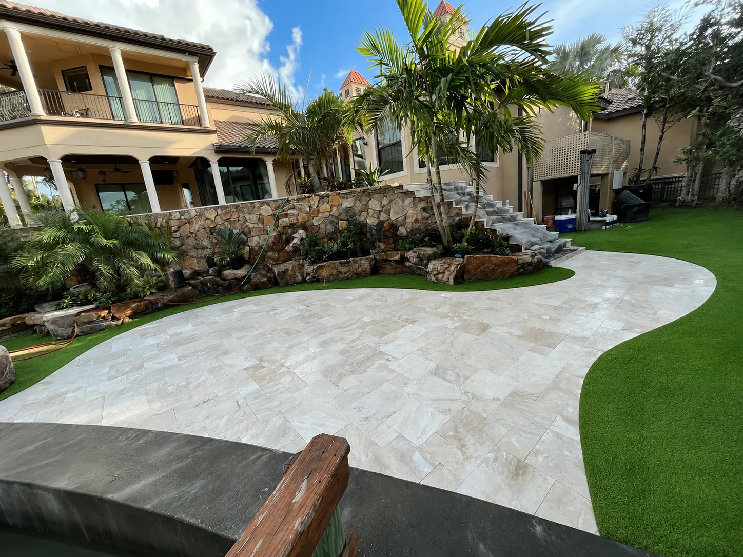 Finished light travertine walkway surrounded by artificial turf and landscaping in Tampa Bay