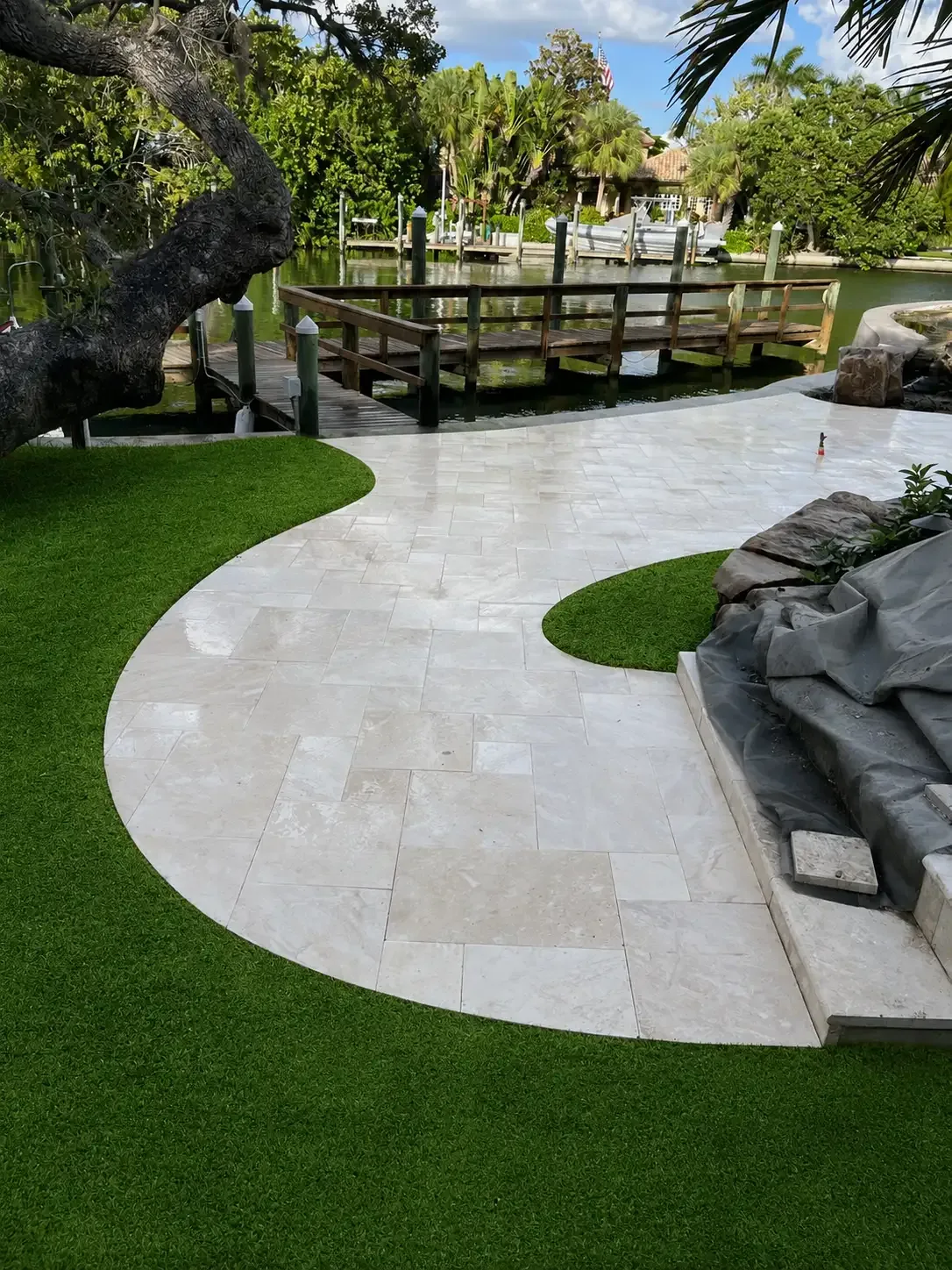 Curved light marble walkway bordered by artificial turf at a waterfront Tampa Bay property