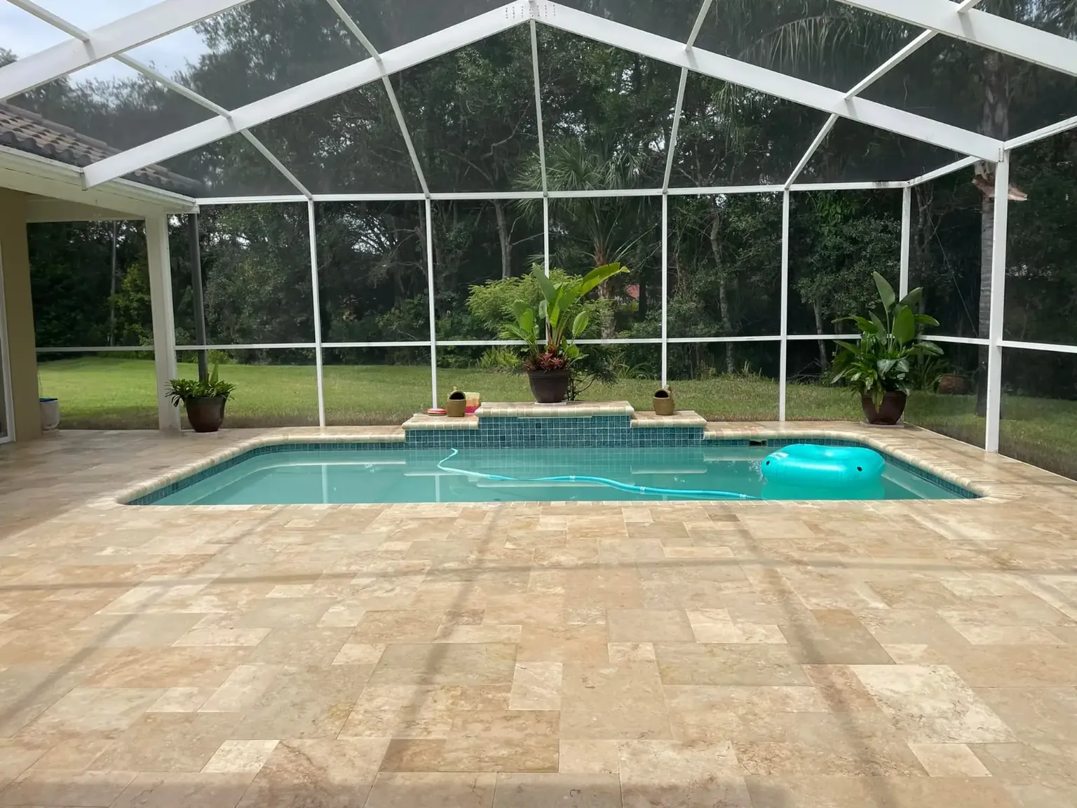 Completed beige travertine pool deck inside a screened residential pool enclosure in Tampa Bay
