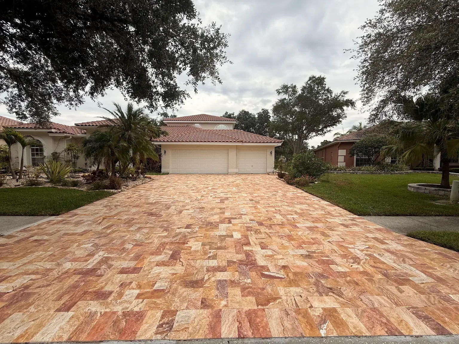 Wide street view of a completed warm tan and rust travertine driveway in Tampa Bay